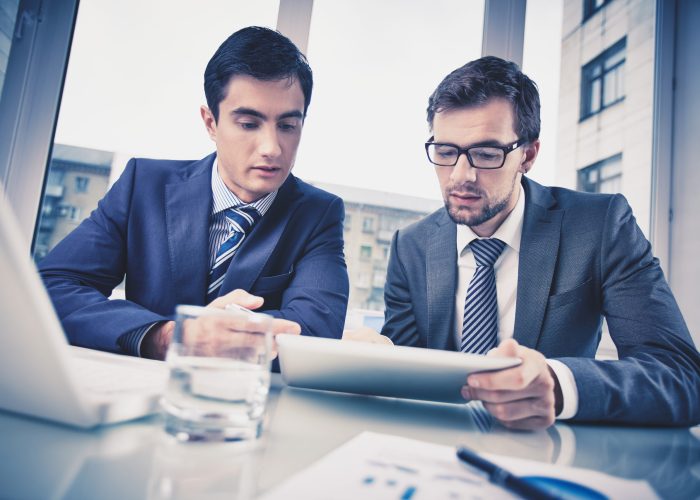 Image of two young businessmen discussing document in touchpad at meeting